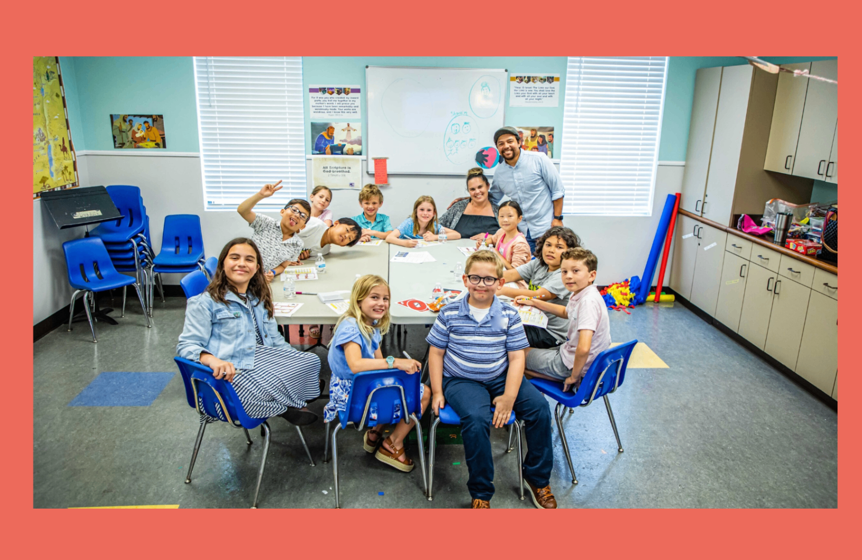 Kids classroom with children gathered around tables and leaders smiling