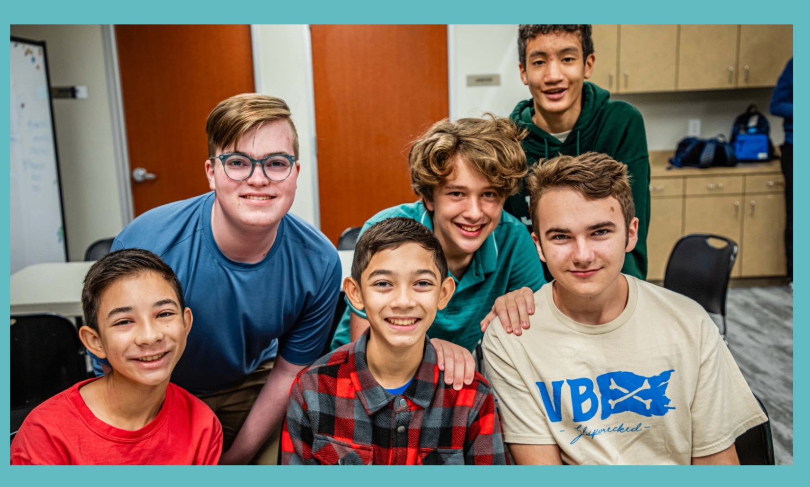 Middle and high school students smiling together in a classroom